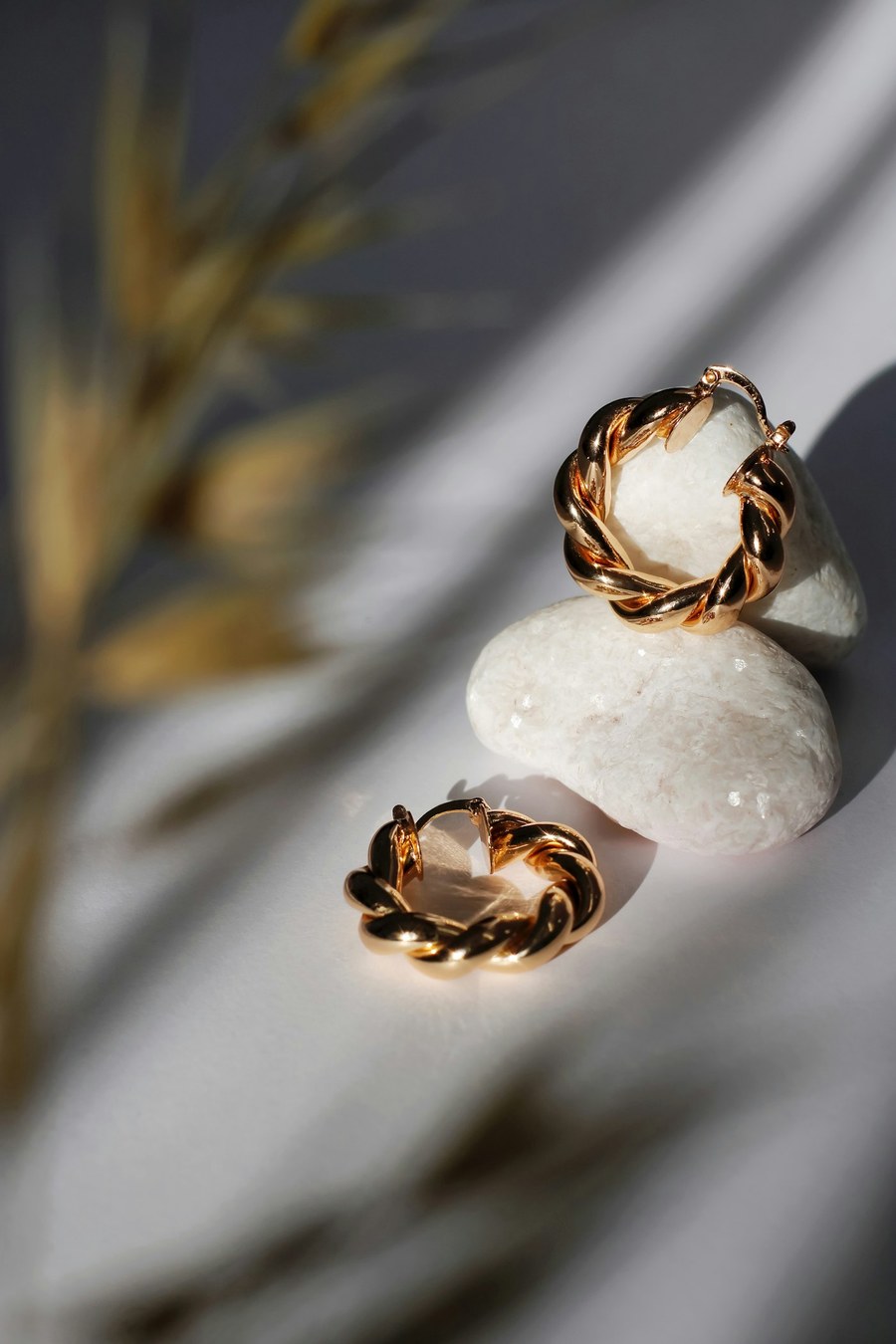 Gold hoop earrings styled on stones in soft light
